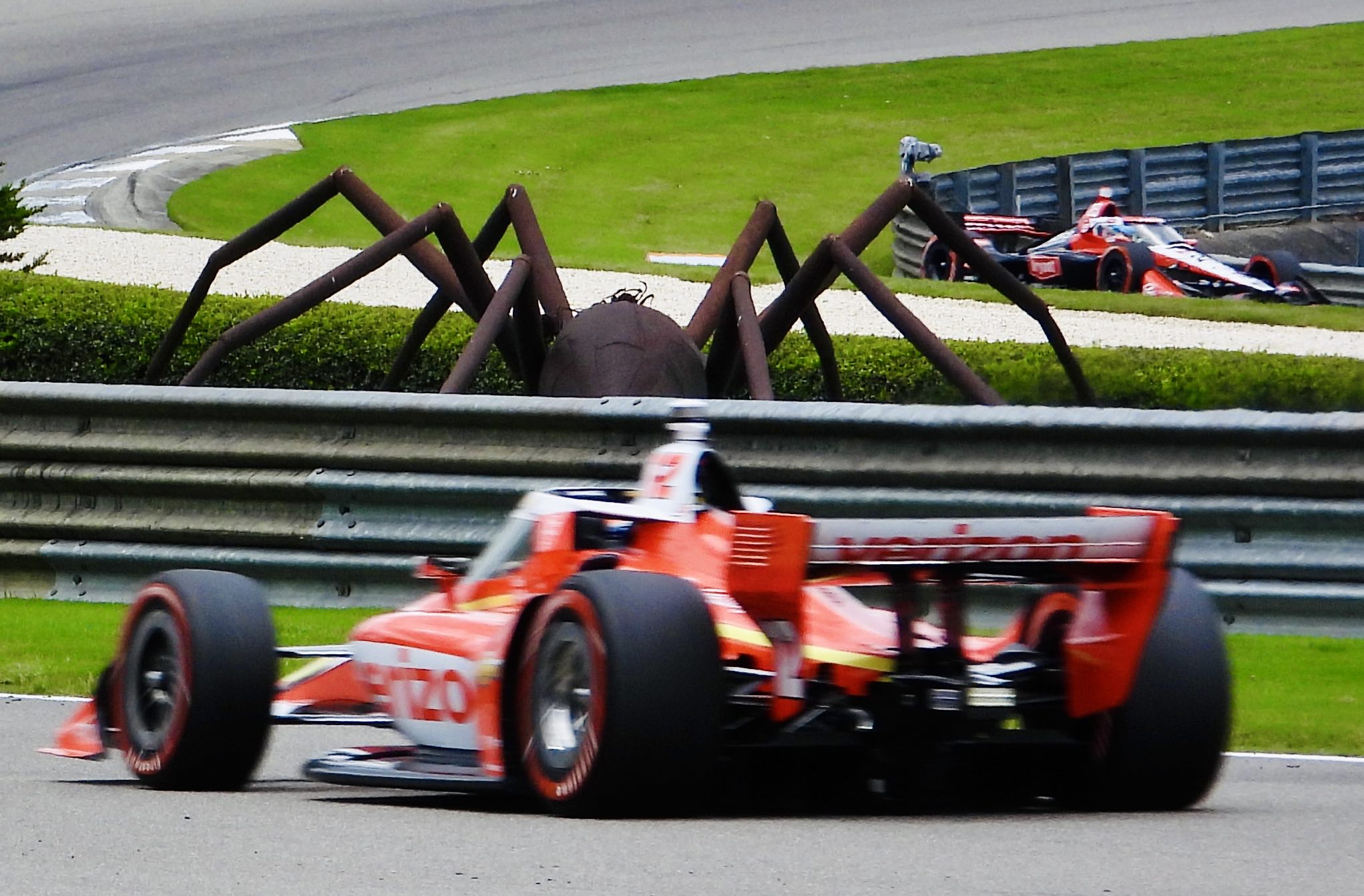 Two Indy cars racing past the giant spider in the infield of Barber Motorsports Park