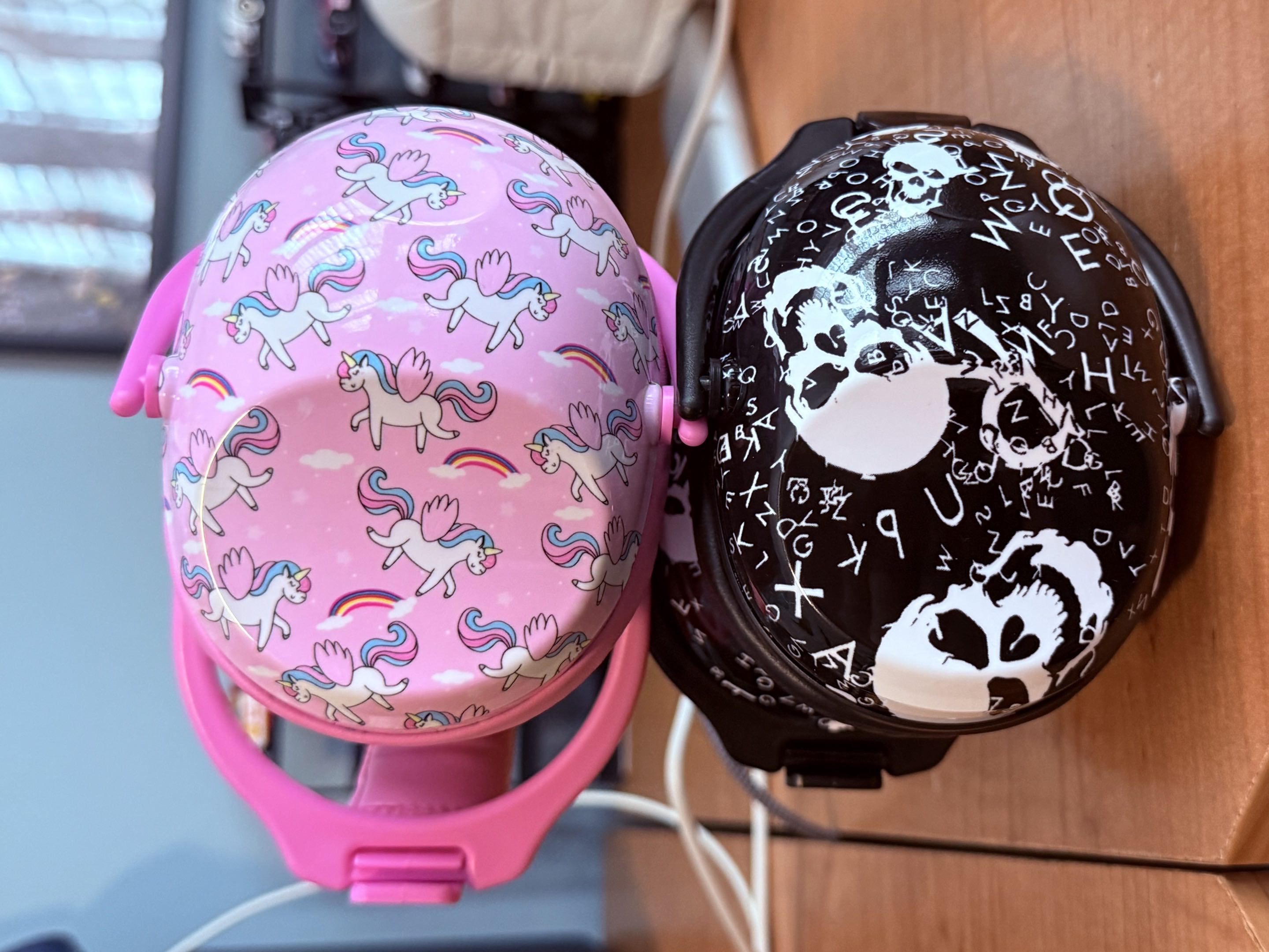 Two sets of children’s noise protection earmuffs, one black with skulls on it, and one pink with unicorns on it