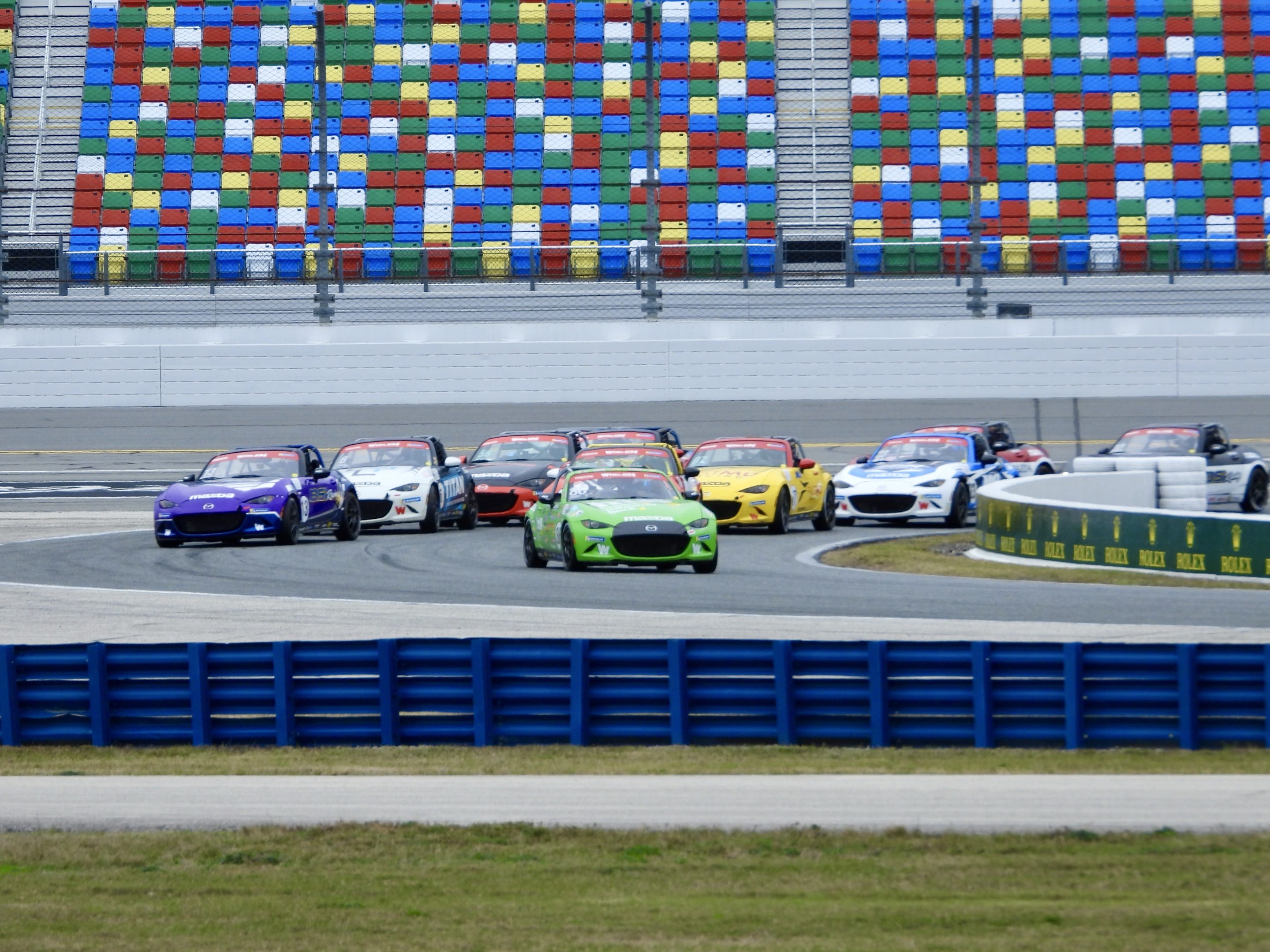 Tiny, colorful race cars going around a bend in front of empty but colorful grandstand seats