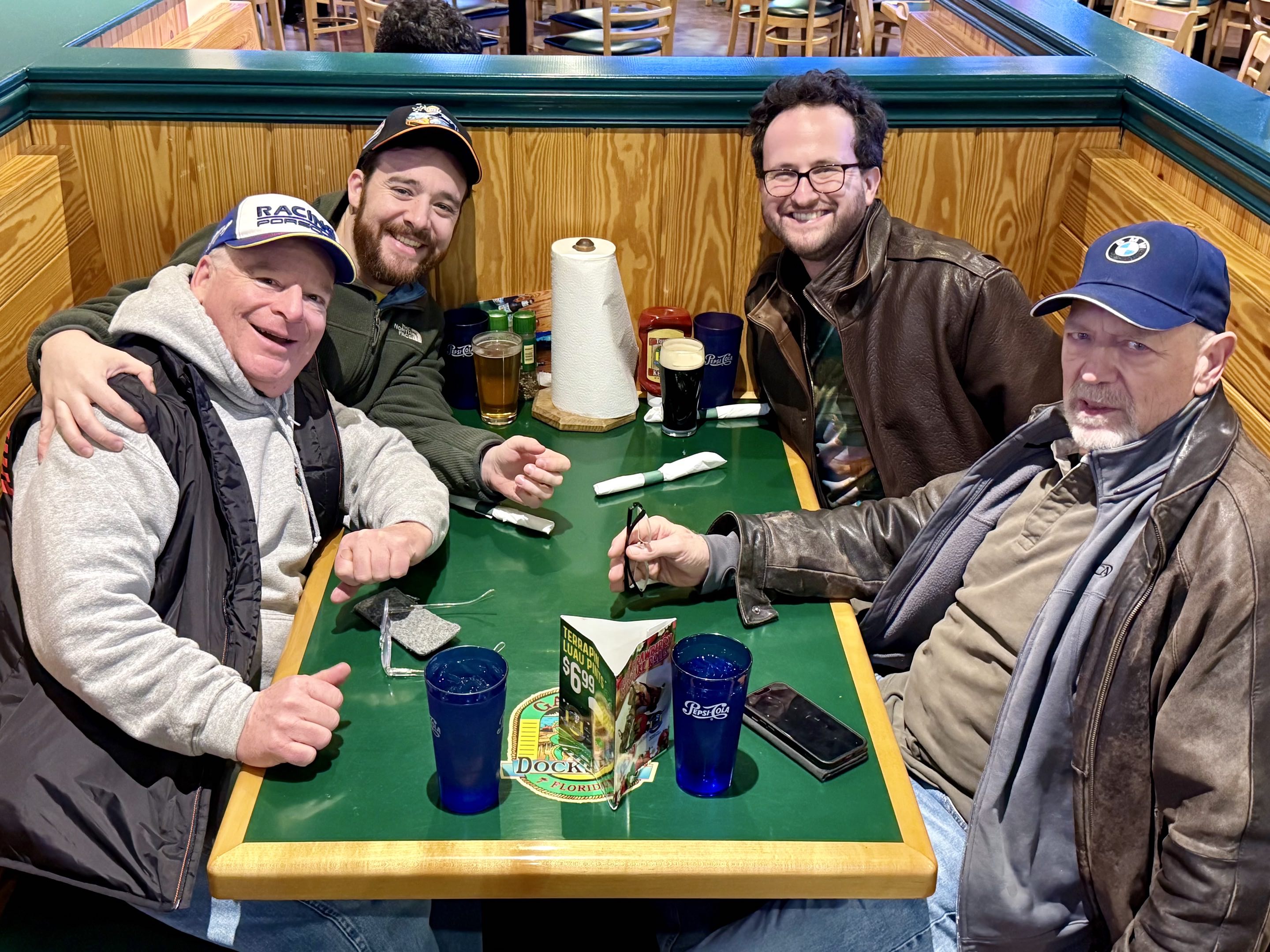 Two thirtysomething men and two of their elders in motorsports fan outfits sitting at a table in a Florida restaurant