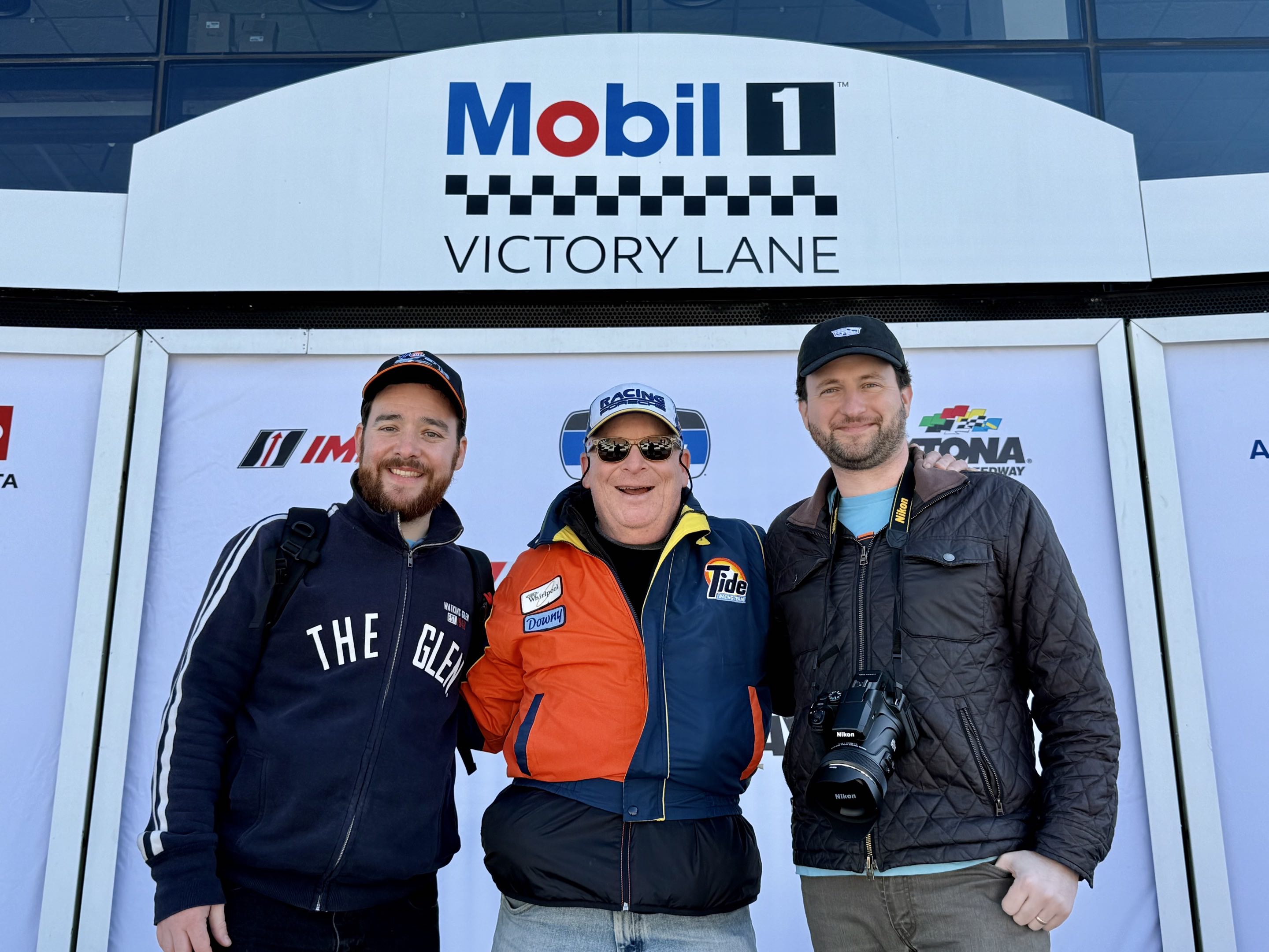 Three men embracing on the podium in Victory Lane at Daytona International Speedway