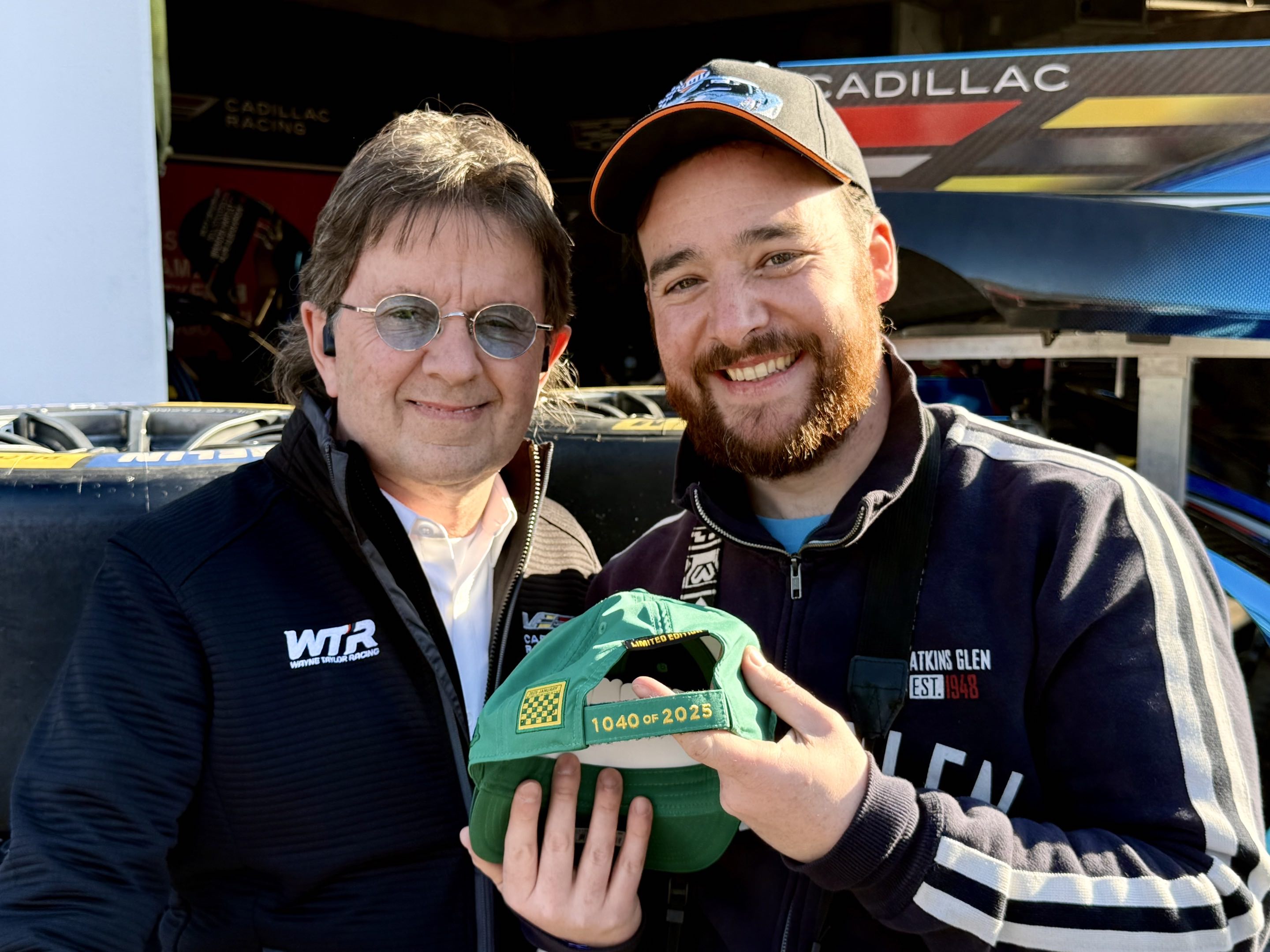 Two men smiling and holding a baseball hat