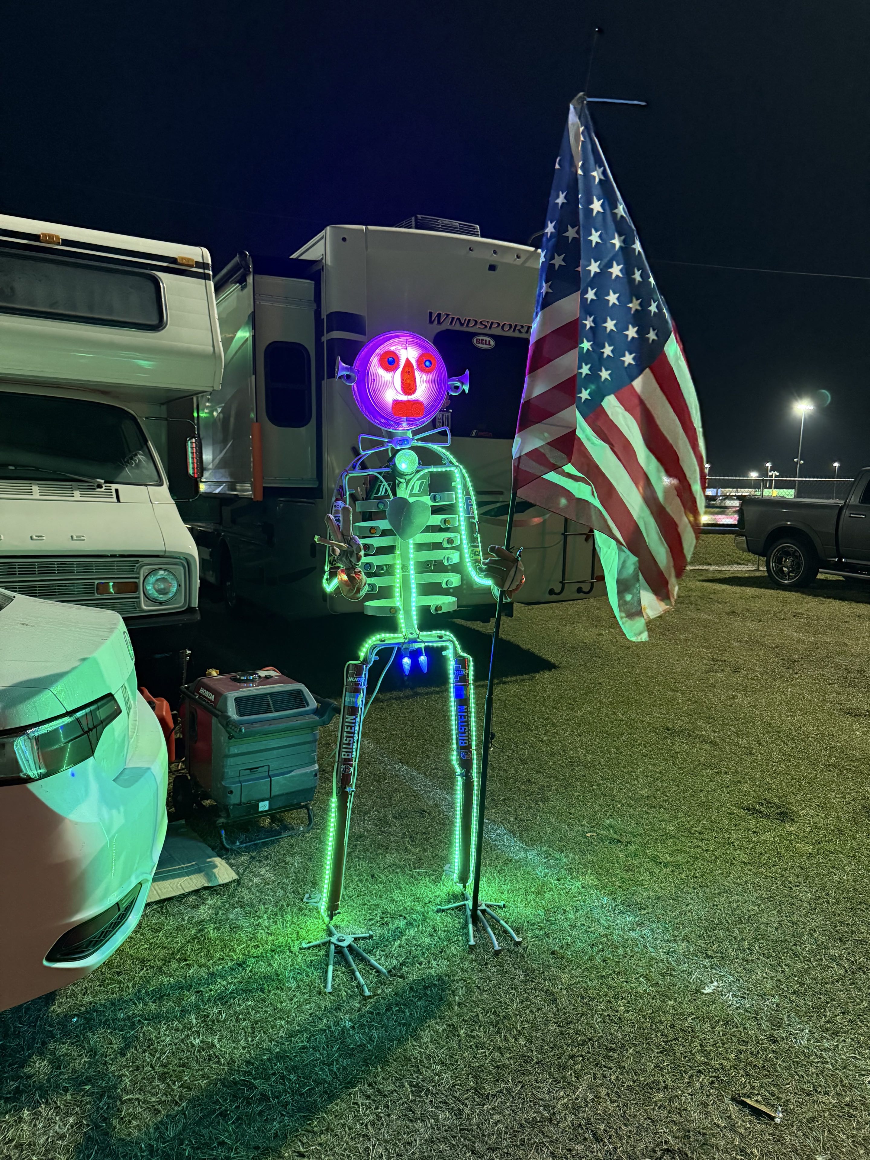 A different strange folk art statue in front of a different car camping site in the nighttime