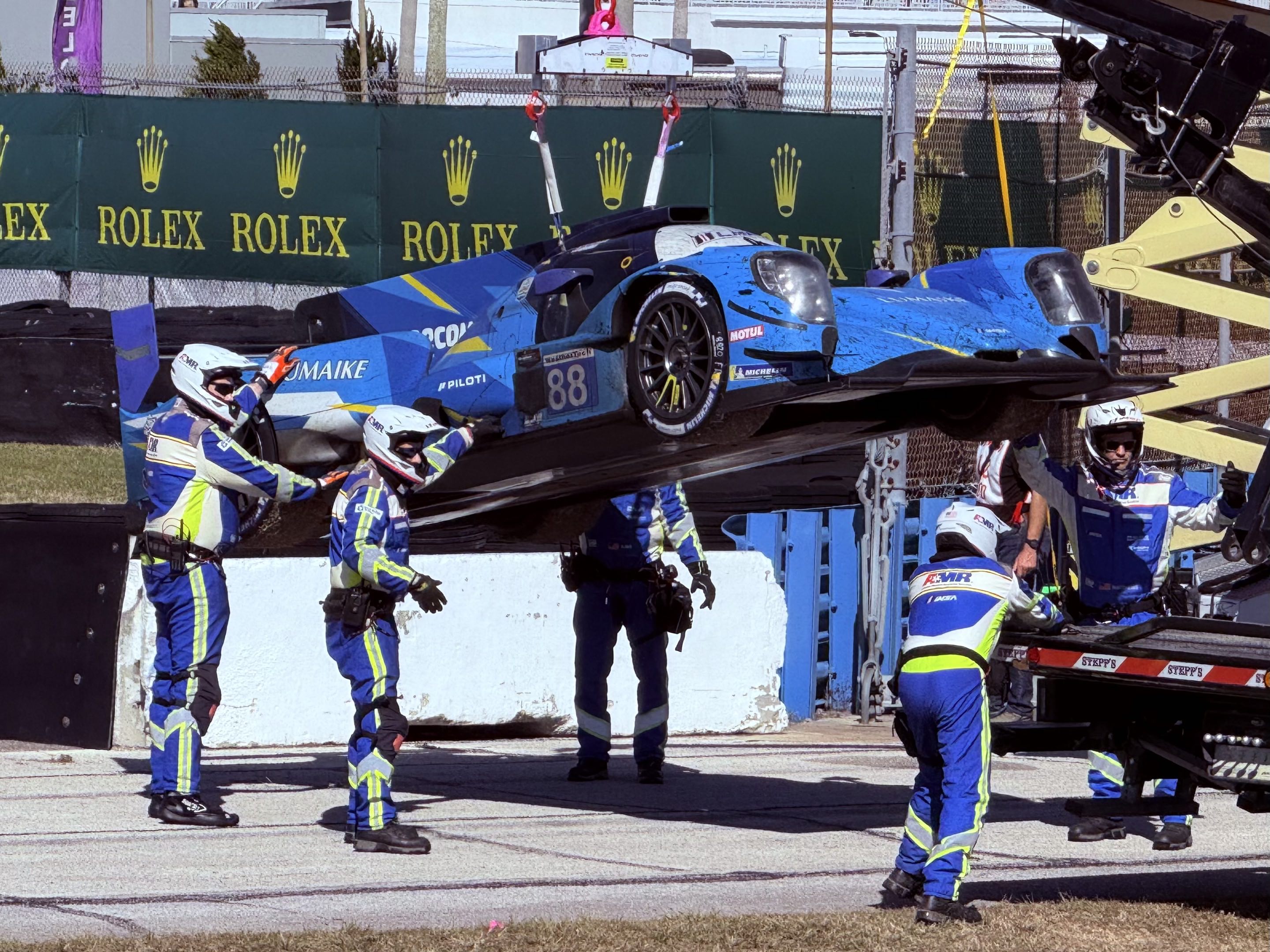 An LMP2 race car gets hoisted off the track by a recovery crew