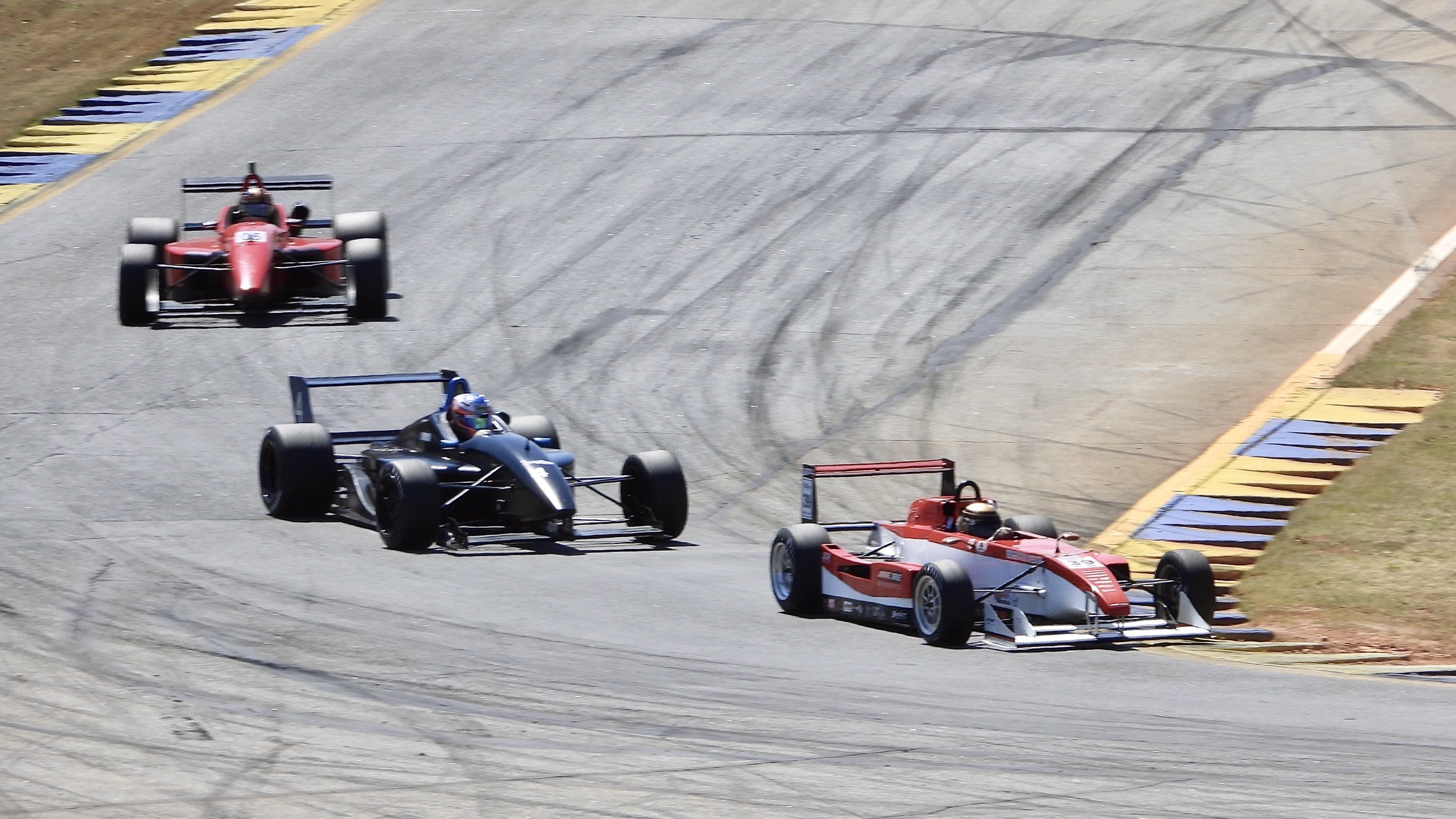 Three small open-wheel race cars going through a downhill left turn