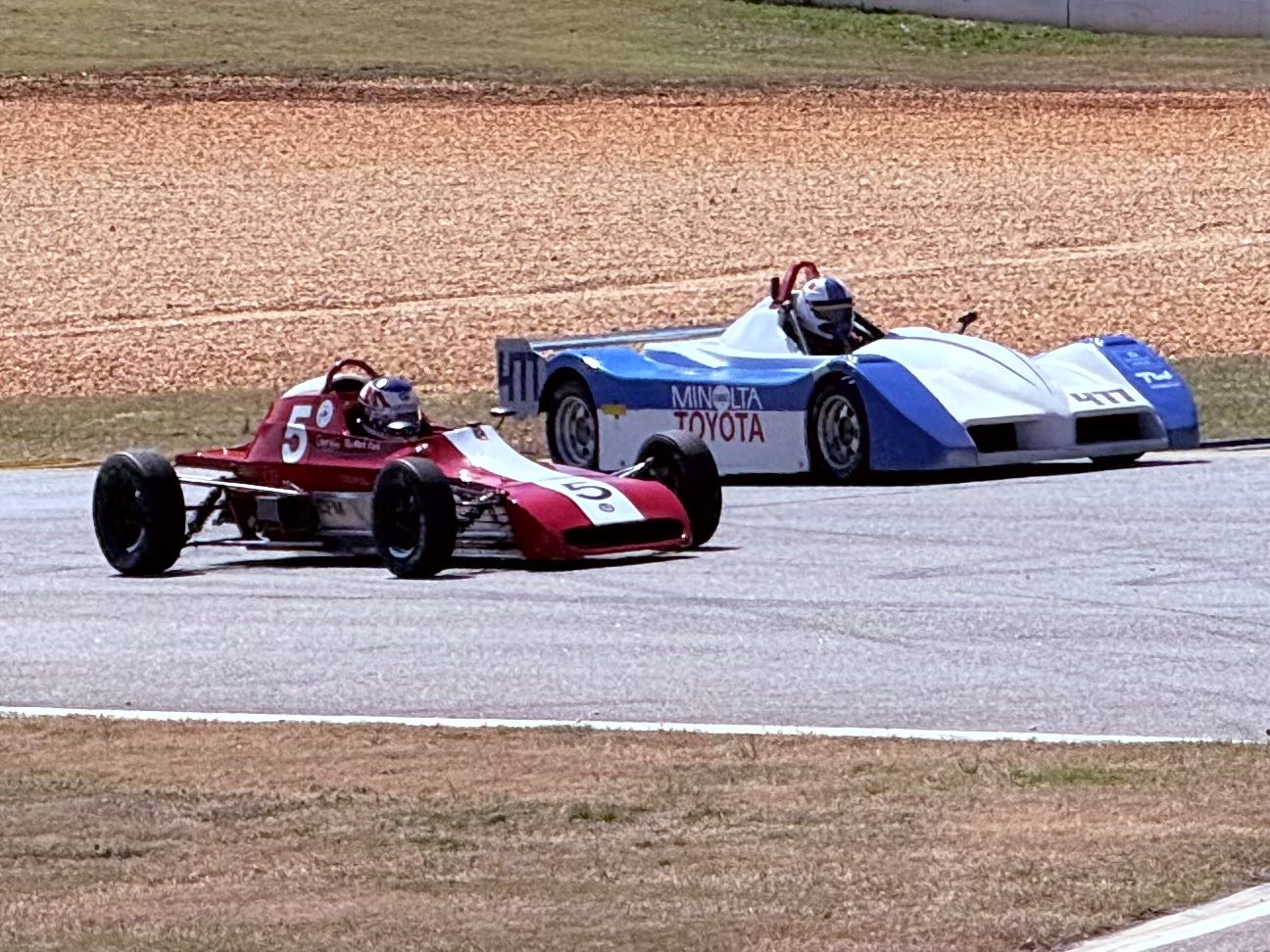 A tiny open-wheel race car and a tiny open-cockpit prototype racing wheel to wheel